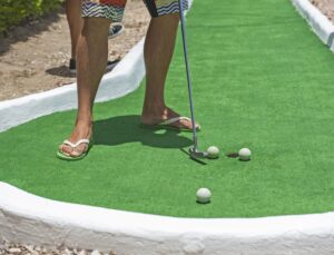Person playing mini golf putting at the hole OBX