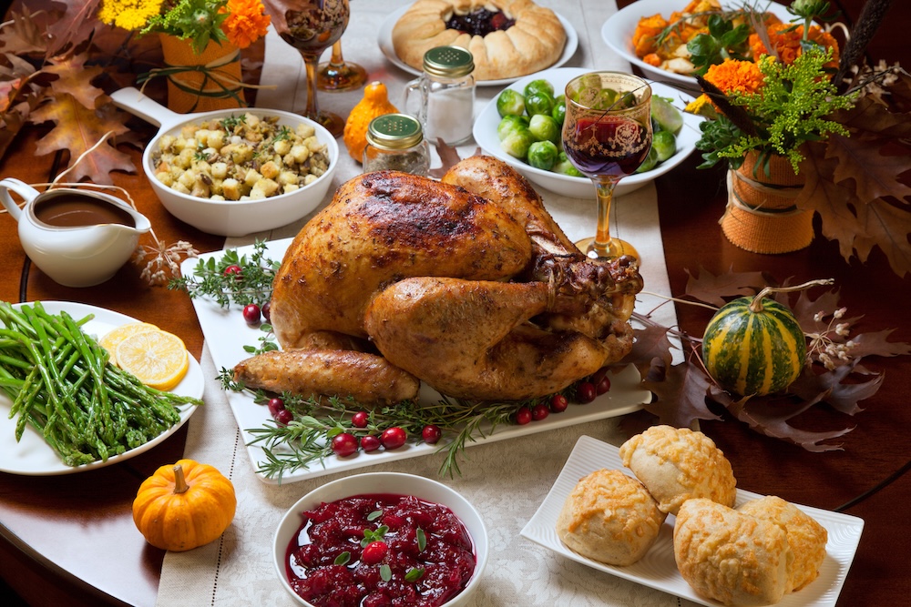 Roasted turkey garnished with cranberries on a rustic style table decoraded with pumpkins, gourds, asparagus, brussel sprouts, baked vegetables, pie, flowers, and candles.